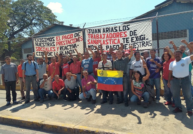 Grupo de trabajadores de Saniplástica, junto a miembros de Aporrea y a visitantes solidarios, con pancartas de lucha al fondo