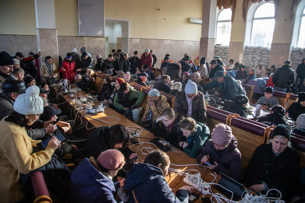 Civiles que huyen de la guerra en Ucrania cargan sus teléfonos móviles y usan wifi en la estación de tren de la ciudad de Jersón. Ese conflicto ha obstaculizado la exportación de cereales y otros rubros, lo que incide en el precio y el acceso a los alimentos y con ello en el hambre en varias regiones del mundo. Imagen: Oleksandr Ratushniak / Unocha